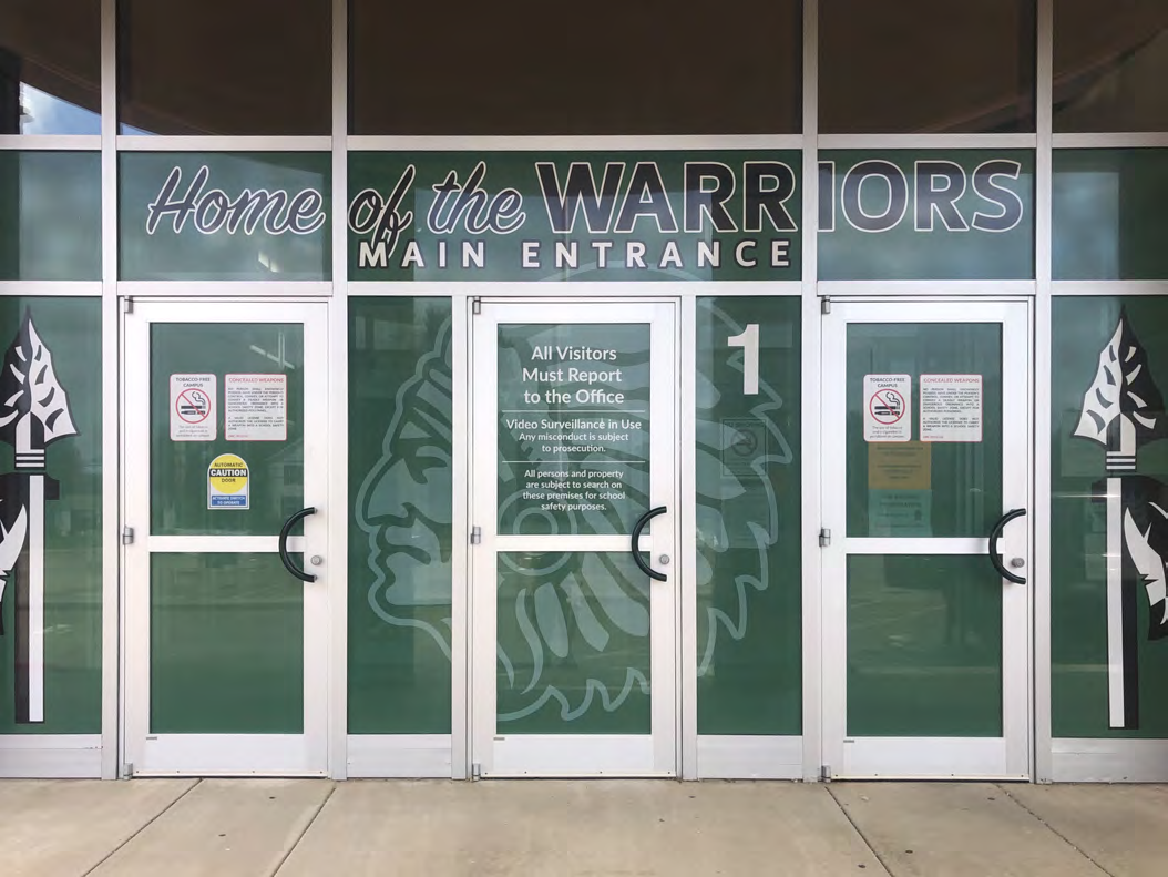 Green school entrance window graphics featuring a Warriors mascot and main entrance lettering